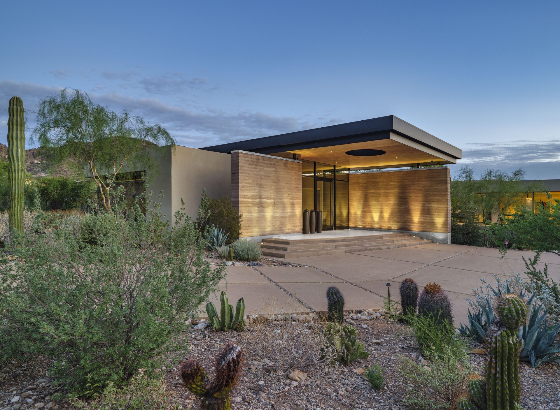 A modern desert residence with rammed earth entry at dusk